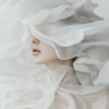 A serene figure draped in translucent white fabric, softly illuminated, creating a dreamlike atmosphere of mystery and elegance.