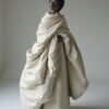 A striking fashion portrait featuring a model enveloped in an oversized garment, highlighting her natural beauty, confidence, and elegance, with a soft, sculptural effect.