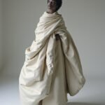 A striking fashion portrait featuring a model enveloped in an oversized garment, highlighting her natural beauty, confidence, and elegance, with a soft, sculptural effect.