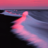 Ocean waves gently meeting a dark sandy shore at sunset, with pink and purple hues in the sky reflecting on the water, capturing the tranquil beauty of the coastline at dusk.