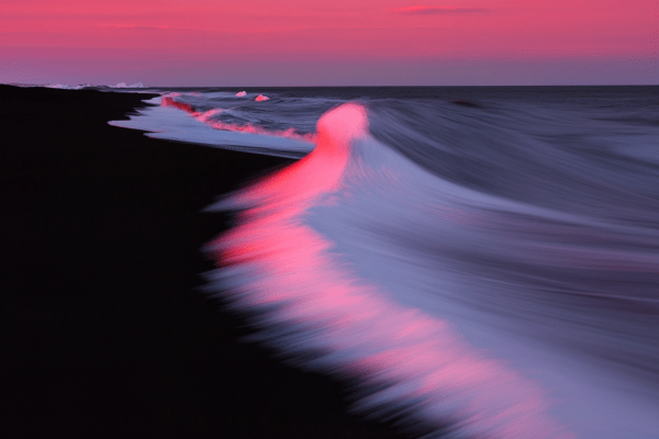 Ocean waves gently meeting a dark sandy shore at sunset, with pink and purple hues in the sky reflecting on the water, capturing the tranquil beauty of the coastline at dusk.