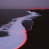 A coastal scene at dusk with gentle waves meeting a dark beach, illuminated by red light. Ice formations rise in the distance, creating a serene yet mysterious atmosphere.