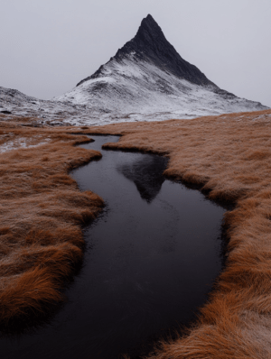 A breathtaking mountain peak with a serene stream, muted grass tones, and a snow-dusted summit, creating a tranquil yet powerful scene.