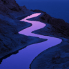 A winding waterway reflects soft purples and blues of twilight, cutting through rugged terrain, creating a serene and peaceful atmosphere in the landscape.