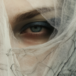 An intimate close-up of a single eye partially veiled by delicate fabric, reflecting emotion and introspection, with soft light and shadow enhancing the mystery of identity.